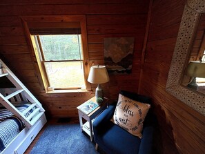 A cozy room with a bunk bed, a small table with a lamp, and a blue sofa with a decorative pillow.