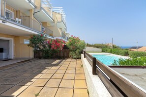 Un edificio residencial con piscina, patio con baldosas y vistas al mar.