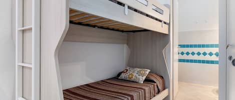 A bunk bed room with a door, a patterned bedspread, and a small pillow.