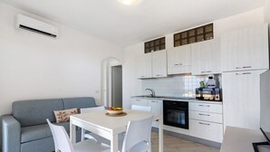 Una cucina compatta con mobili bianchi, forno integrato e macchina per il caffè.