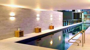 A modern indoor swimming pool with a tiled floor, a long bench, and wall-mounted lights. - CASA DELUXE #5 - Pool Gym Sauna Spa City Views Parking (South Yarra)