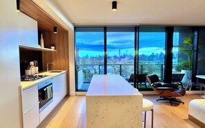 Eine moderne Küche mit einer großen Kochinsel, einem Essbereich mit Stühlen und Blick auf die Stadt durch große Fenster.