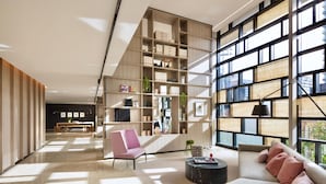 A modern living room with a large bookshelf, a sofa, a coffee table, and a view through large windows. - CASA DELUXE #5 - Pool Gym Sauna Spa City Views Parking (South Yarra)