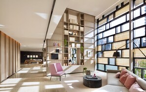 Ein modernes Wohnzimmer mit einer großen Bücherwand, einem Sofa, einem Couchtisch und Blick durch große Fenster.