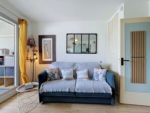 A cozy living room with a sofa, a framed picture, a mirror, and a door with a unique design. - La Santa Maria by Interhome (Port Camargue)