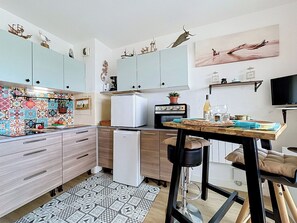 A modern kitchen with light blue cabinets, a small refrigerator, a coffee maker, and a dining area with a table and chairs. - La Santa Maria by Interhome (Port Camargue)