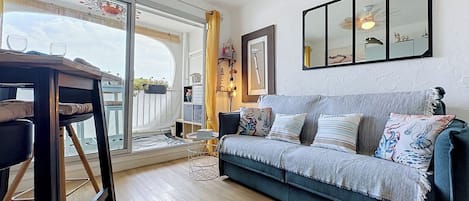 Un salon comprenant un canapé, une table basse, un fauteuil, une grande fenêtre et un ventilateur de plafond.