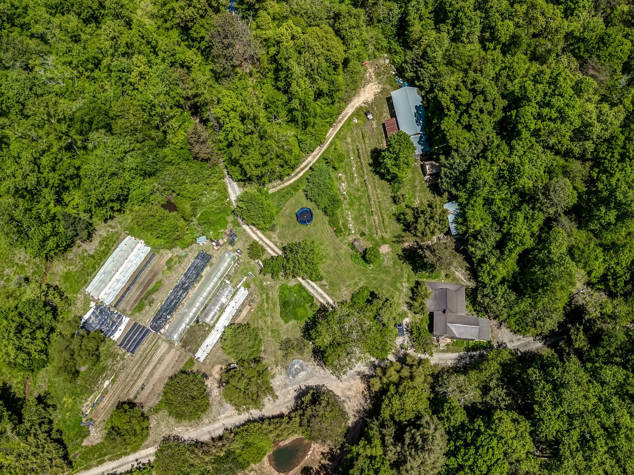 An aerial view of a property with a large greenhouse, a small building, and a pond.