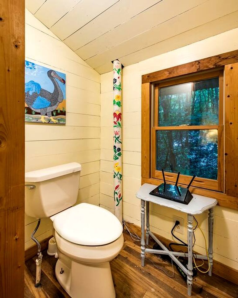 Casa de banho com sanita, janela com vista para uma floresta e parede com padrão colorido.