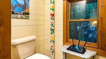 Casa de banho com sanita, janela com vista para uma floresta e parede com padrão colorido.