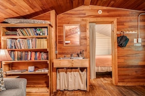 A cozy cabin with a wooden interior, a bookshelf filled with books, a small kitchenette, and a bed with a curtain.