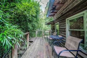 A wooden deck with a table and chairs, surrounded by dense foliage.