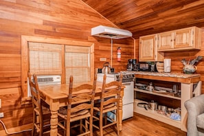 A wooden interior with a dining table, chairs, a stove, and kitchen cabinets.