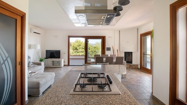 Una cocina moderna con estufa a gas, techo de vidrio, un espacio de descanso con sofá y vistas a través de un ventanal.