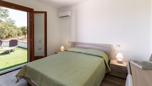 Un dormitorio con cama, lámparas de noche, mesita de noche, ventana con vista a un jardín y un equipo de aire acondicionado.