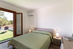 Ein Schlafzimmer mit einem Bett, Nachttischlampen, einem Beistelltisch, einem Fenster mit Gartenblick und einer Klimaanlage.