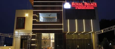 A hotel with a modern facade, a prominent sign reading 'Royal Palace Banquet Hall,' and a visible entrance with a glass door.