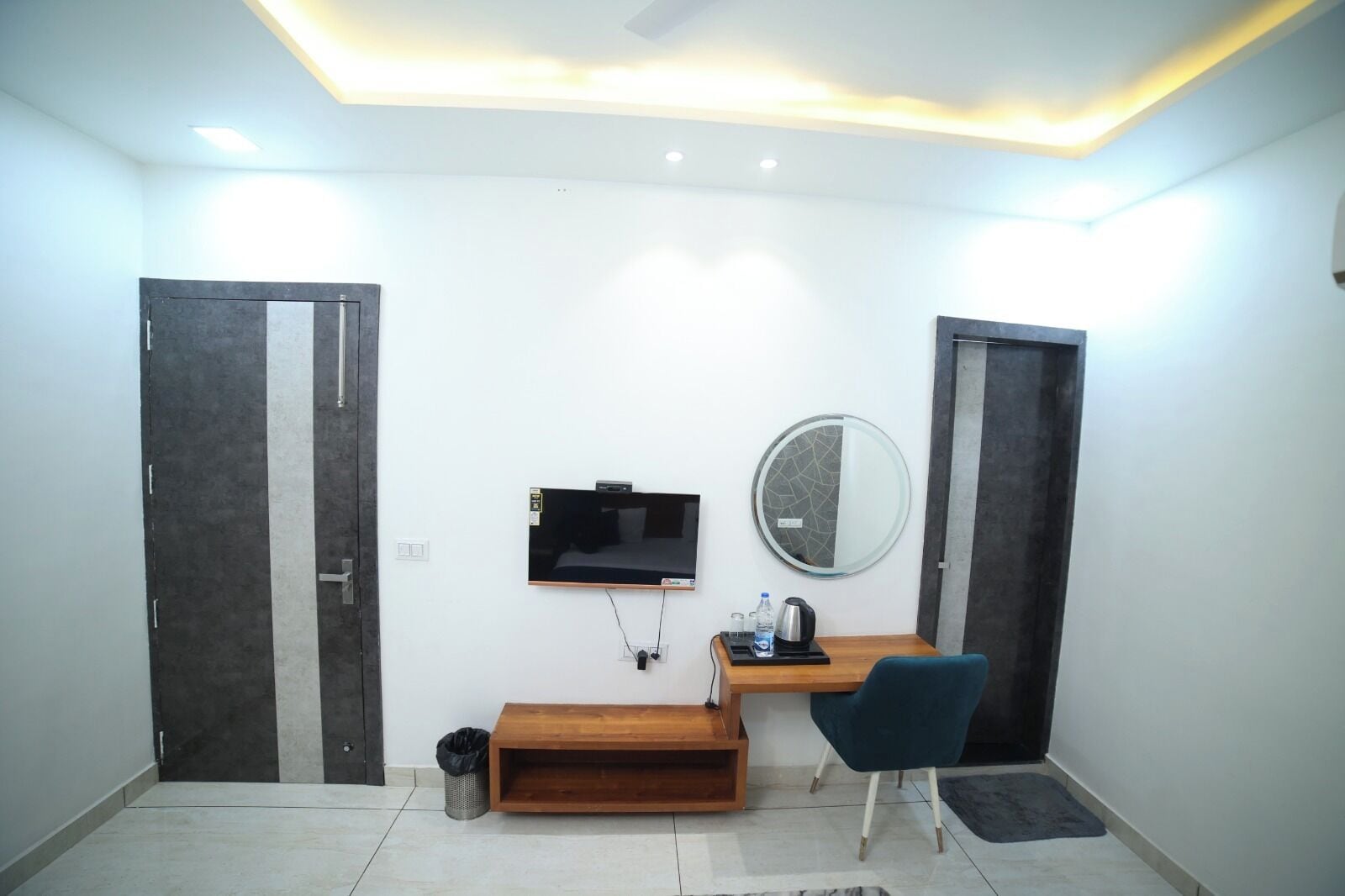 Habitación de hotel con escritorio, silla, televisor, espejo y dos puertas.