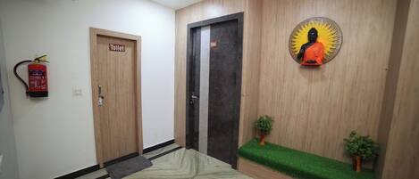 A hallway with a wooden door labeled 'Toilet,' a fire extinguisher, a door with the number '104,' and a statue on the wall.