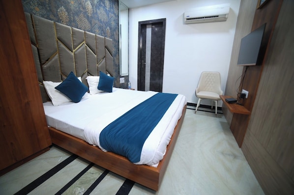 A bedroom with a bed, pillows, a chair, a TV, and an air conditioning unit.