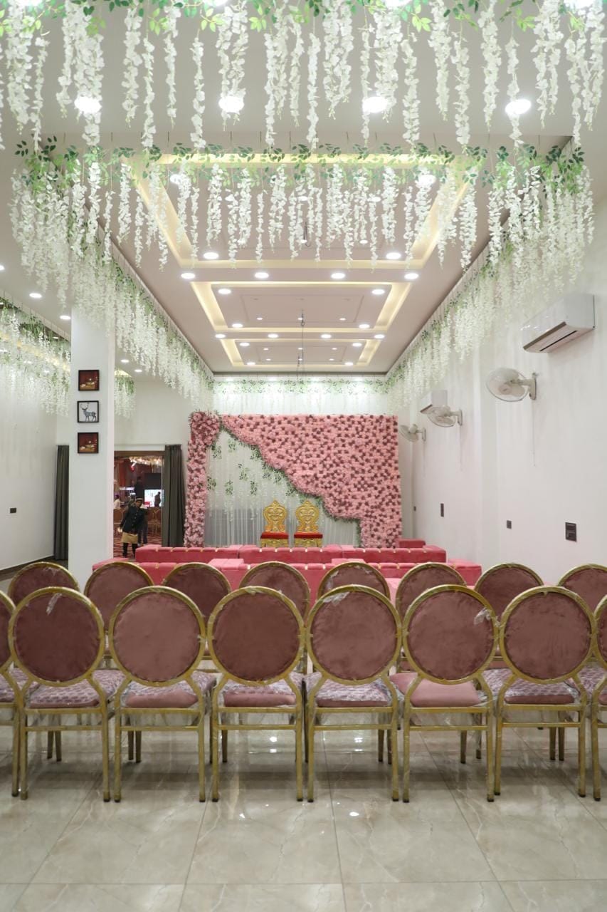 Un salón de conferencias con un escenario, sillas y plantas colgantes decorativas.