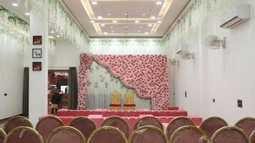 Un salón de conferencias con un escenario, sillas y plantas colgantes decorativas.