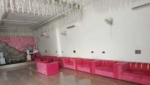 A room with a pink sofa set, a decorative wall with a pink and white pattern, and a ceiling with hanging floral decorations. - HOTEL ROYAL PALACE (Bhiwani)