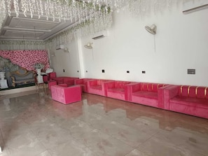 Una habitación con sofá rosa, pared decorada con un estampado rosa y blanco, y techo con adornos florales colgantes.
