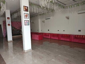 A spacious lobby with a long row of red sofas, a tiled floor, and hanging floral decorations. - HOTEL ROYAL PALACE (Bhiwani)