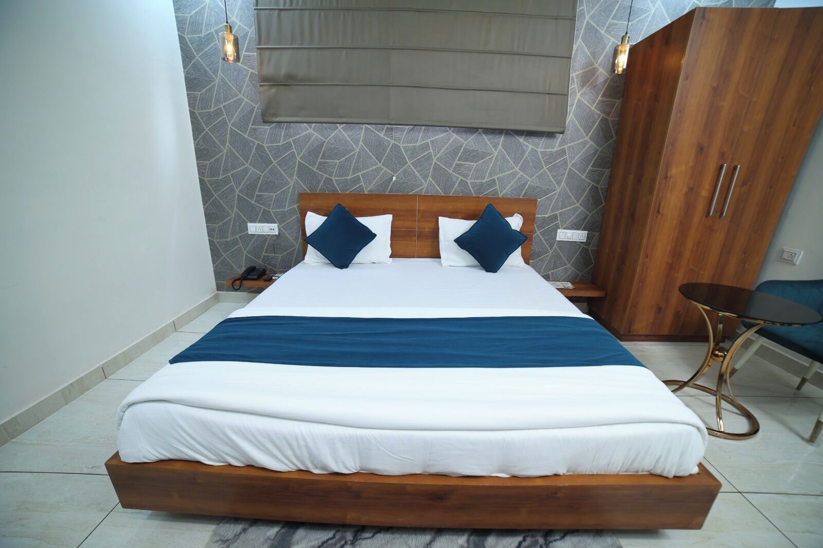 Una habitación de hotel moderna con una cama grande, cabecero de madera, una mesita y un armario.