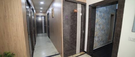 A hallway with wooden paneling, a marble floor, and doors marked with room numbers.
