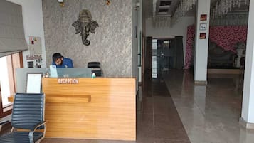 En receptionsdisk med en receptionist, en vägg med ett mönster och en kristallkrona.