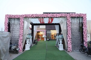 Una entrada decorada con una alfombra verde que conduce a un edificio, pilares blancos y arreglos florales rosados.