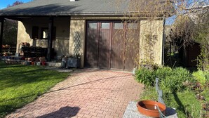 Une maison avec un chemin de briques menant à une porte en bois, entourée de verdure et sous un ciel dégagé.