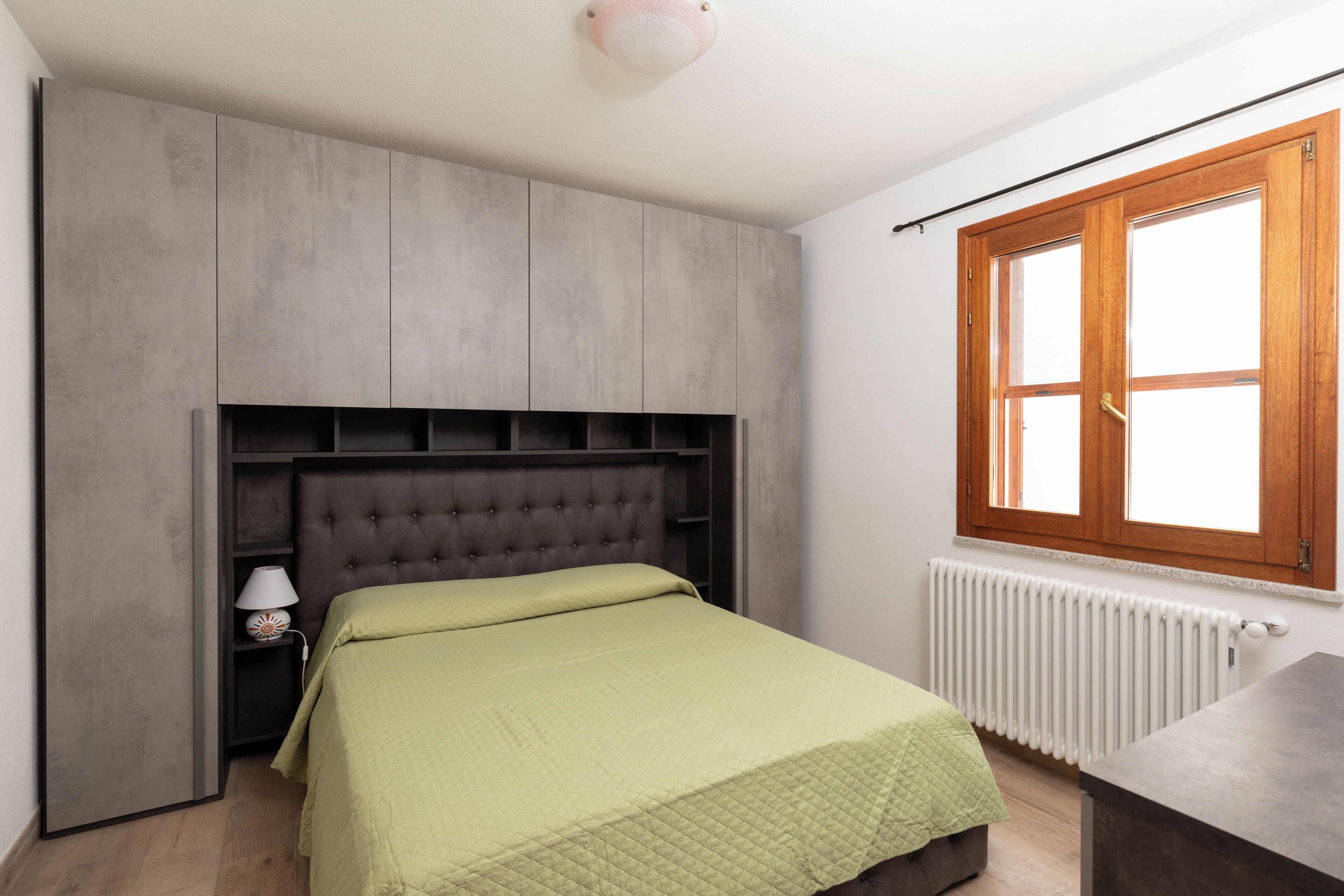 A bedroom with a bed, a nightstand, a dresser, a window, and a radiator.