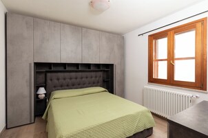 Quarto com cama, mesa de cabeceira, cômoda, janela e radiador.