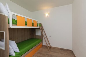 Ein Etagenbett mit einer Leiter, einer grünen Matratze und einer weißen Wand mit einer Leuchte.