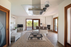 A modern kitchen with a gas stove, a glass shelf, and a dining area with chairs. - Villa Certosina by Wonderful Italy (Siniscola)