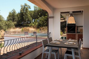 Ein Essbereich im Freien mit Pool, Grill und Blick auf Bäume.