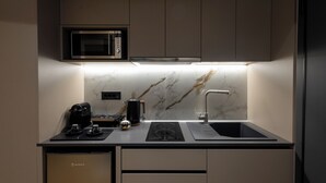A compact kitchen with a microwave, coffee machine, kettle, and a sink. - Lux Suites Athens (Athina)
