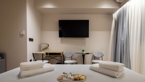 A hotel room with a bed, a desk, two chairs, a flat-screen TV, and a window with curtains. - Lux Suites Athens (Athina)