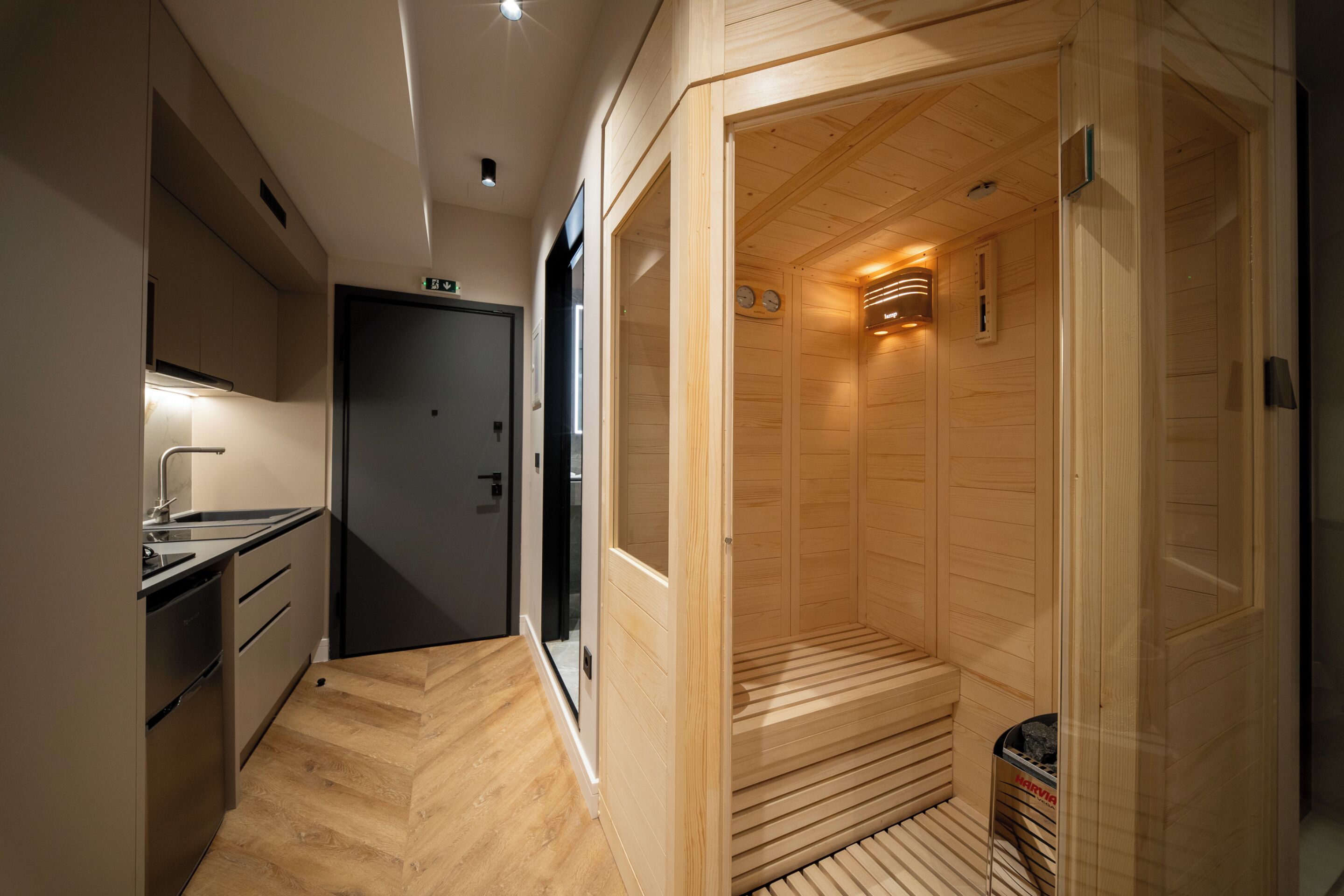 A modern hotel room with a wooden interior, a built-in sauna, and a separate kitchenette area.