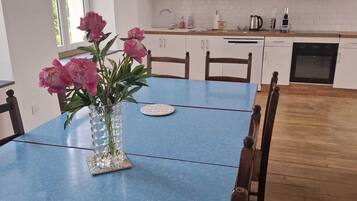 Une table à manger avec des chaises, un vase de fleurs, une horloge et un coin cuisine avec des placards et des appareils électroménagers.