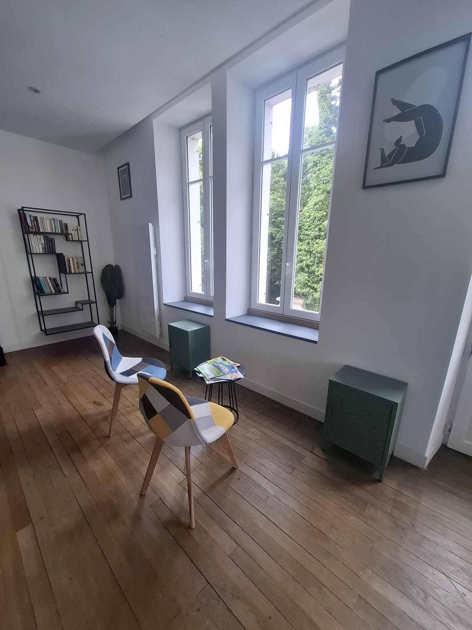Ett rum med en bokhylla, två stolar, ett litet bord och ett fönster med utsikt över grönområden.
