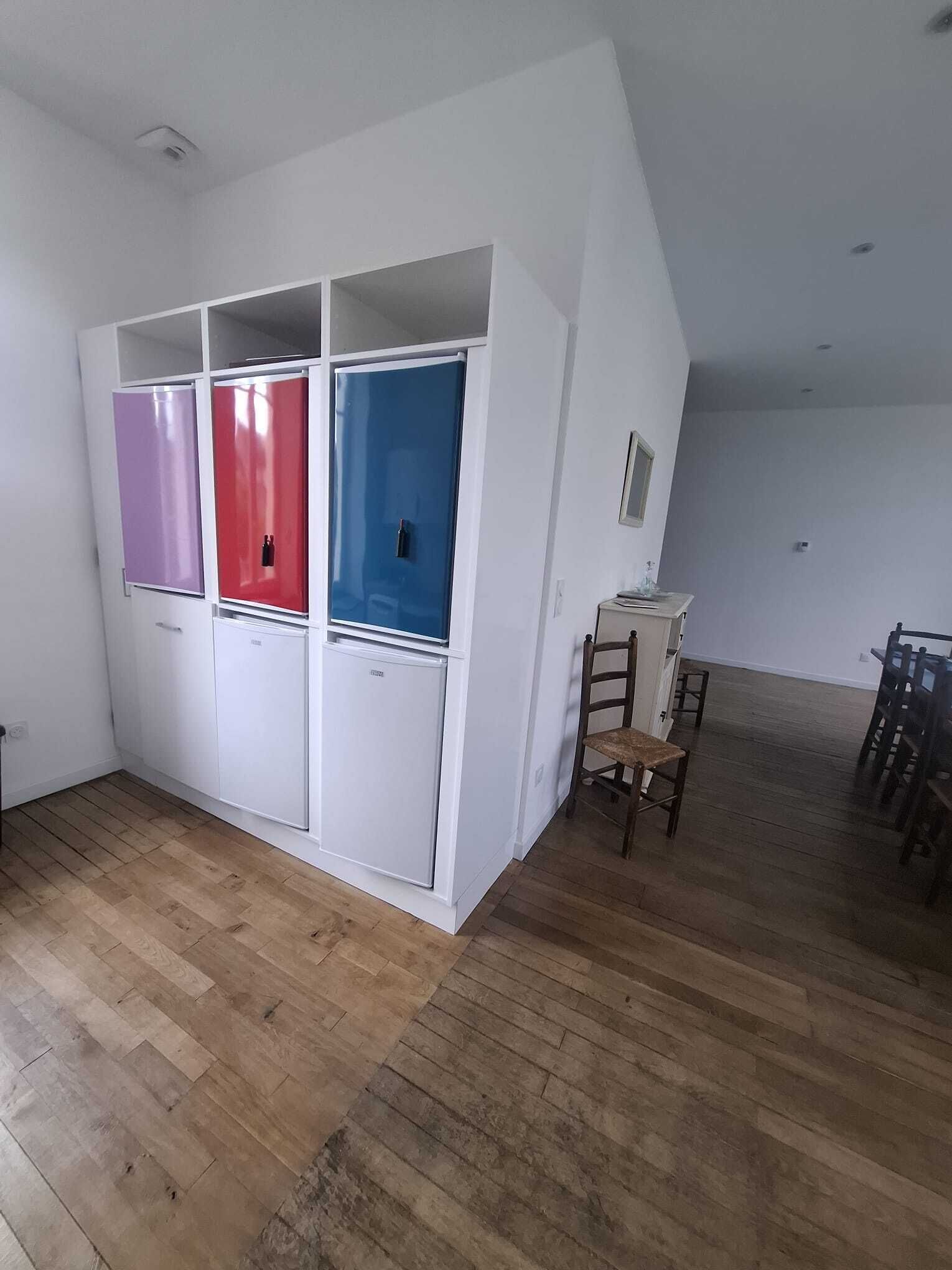 Une pièce avec un plancher en bois, des murs blancs, une armoire blanche à plusieurs portes, une petite table et une chaise.