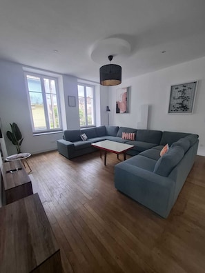 A modern living room with a sectional sofa, a coffee table, and a dining area with a wooden table and chairs. - 200-square-meter apartment - 5 bedrooms - 3 bathrooms (Avallon)