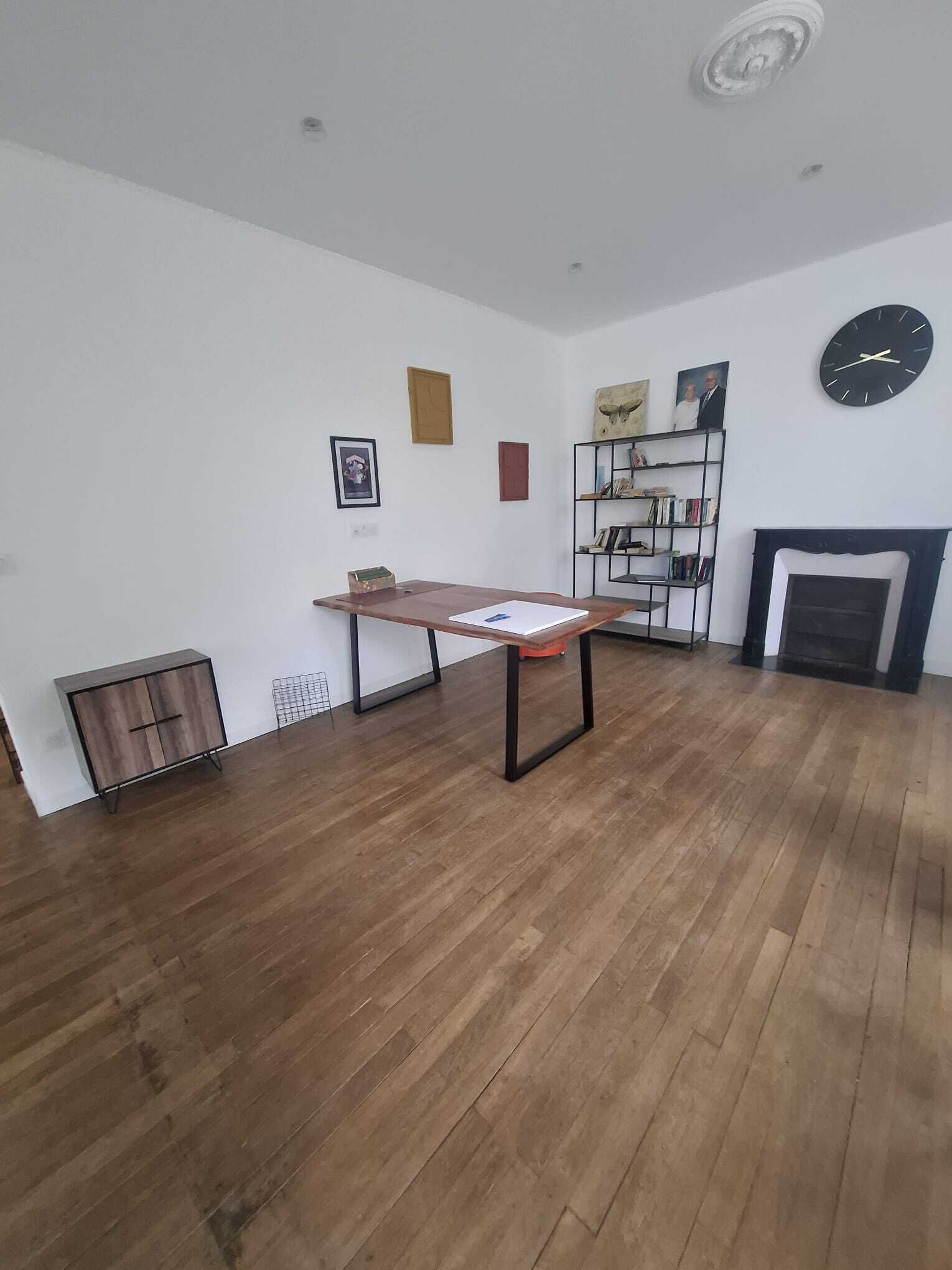 A room with a wooden floor, a table, a bookshelf, and a fireplace.