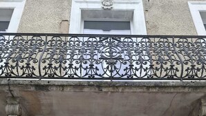 A building facade with a red door, a balcony with ornate metal railings, and a stone plaque with the number 17.