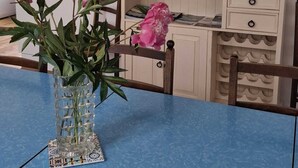 A dining area with a blue table, a vase with flowers, a wooden chair, a white dresser with drawers, and a mirror on the wall.