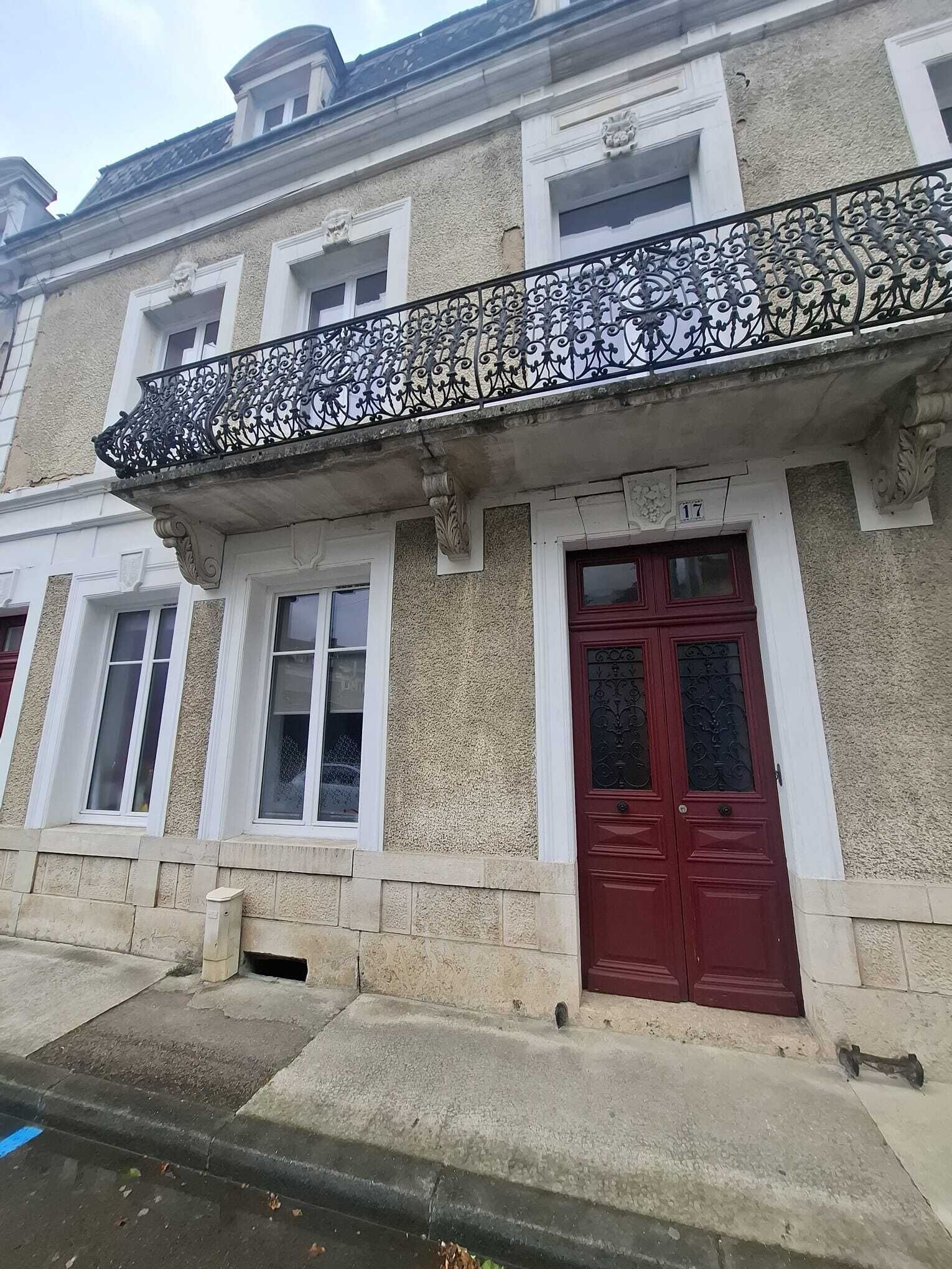 A building with a red door, white-framed windows, and a decorative metal balcony railing.
